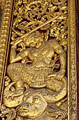 Wat Xieng Thong temple in Luang Prabang, Laos. Detail of a wooden door of the sim with gilded carvings on a red background. 